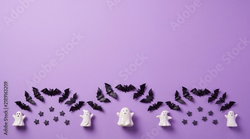 Flat lay of small white ghost figurines and black paper bats arranged on a solid purple background for halloween decorations