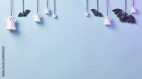 Minimalist halloween background featuring hanging black paper bats and small white ghost ornaments against a plain light blue backdrop wall