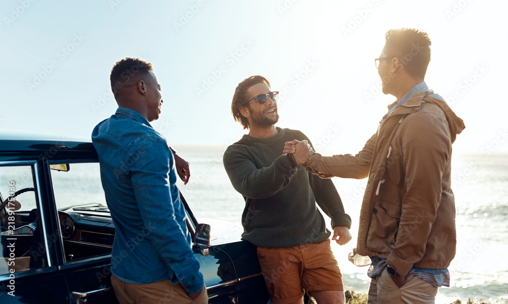 Obraz premium Friends, handshake and road trip with men on coast together for bonding, hangout or social gathering. Greeting, reunion and travel with happy people shaking hands at seaside for holiday or vacation