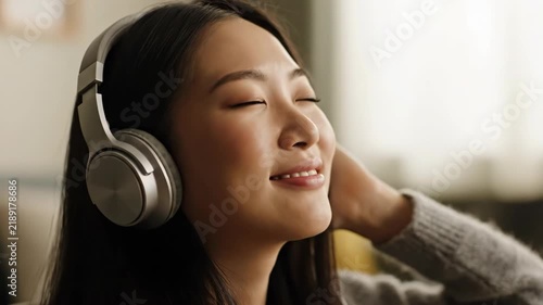 A woman is shown smiling with her eyes closed, wearing silver headphones. She is relaxed