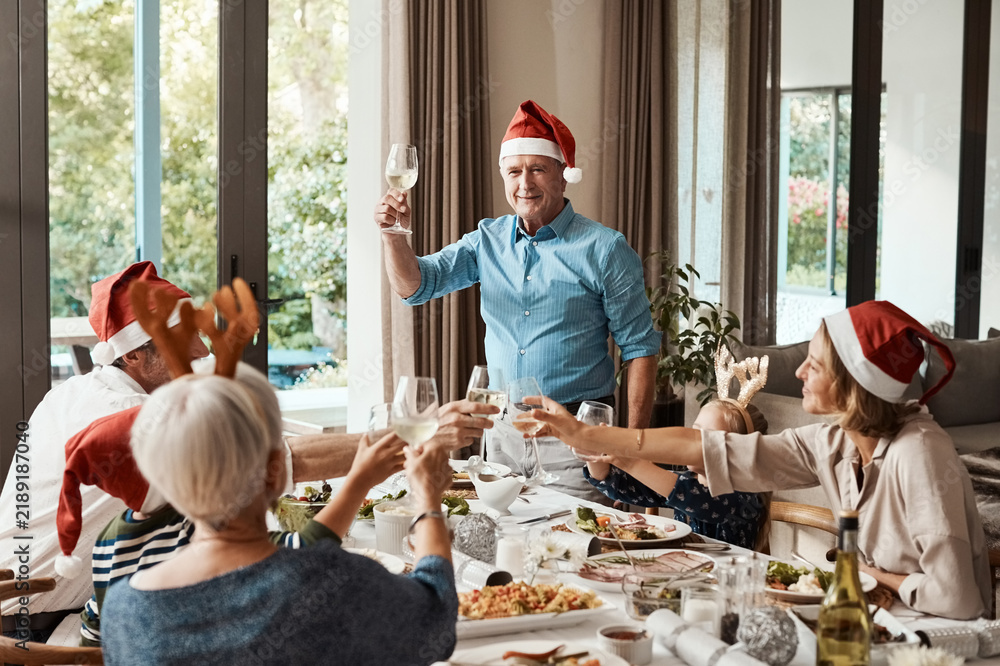 Obraz premium Grandpa, toast and Christmas lunch with family, celebration and festive with drinks in home. Grandparents, parents and children happy for holiday gathering, dinner party and cheers with beverage