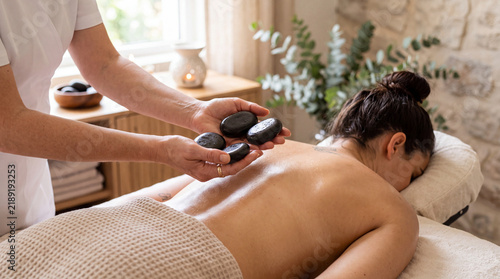 Professional therapist holding dark smooth hot basalt stones for relaxing body massage session