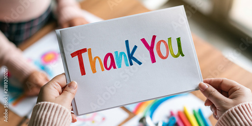 A close-up shot shows hands holding a colorful Thank You card, with a child's artwork visible in the background. This image conveys gratitude and appreciation.