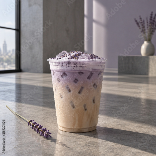 Iced lavender latte in a clear plastic cup with purple foam and dried lavender garnish on a concrete surface with a city view in the background