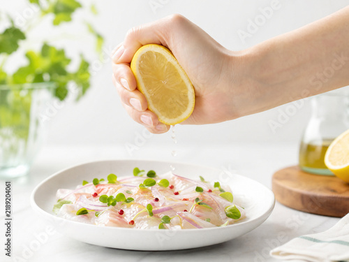 お皿に盛られた魚のカルパッチョに新鮮なレモンを絞る手元