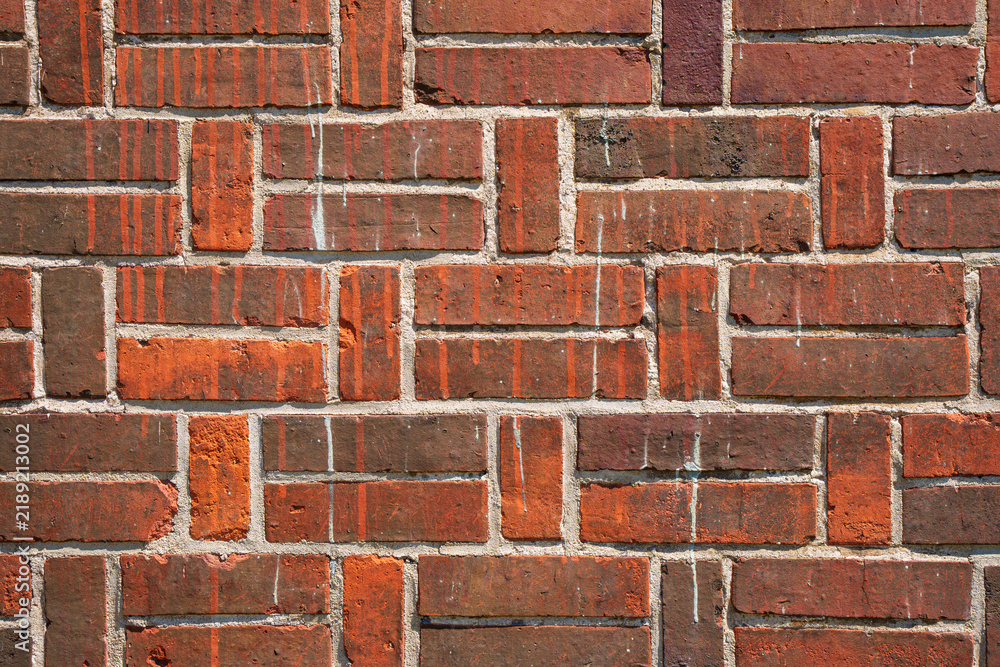 Obraz premium Close-up view of a weathered red brick wall showing rough texture, mortar joints, vertical paint drips and rustic wear - ideal for backgrounds, architecture, construction, and design projects.
