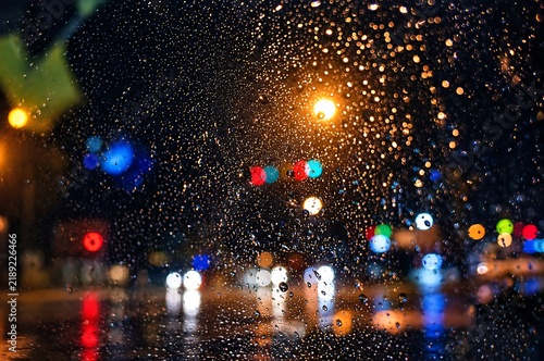 Raindrops on window glass with glowing golden street lights and colorful bokeh at night