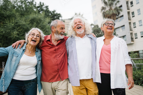 Happy senior friends bonding, walking and laughing together in city park enjoying active retirement