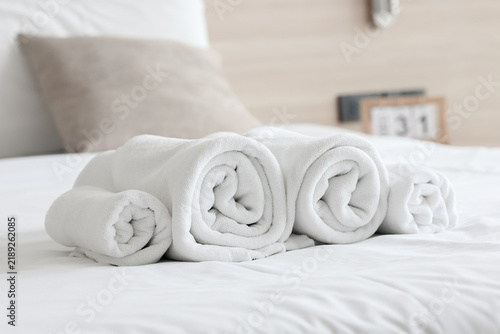 Rolled clean white cotton towels neatly stacked on a soft white bed sheet in a hotel room, symbolizing hospitality, spa relaxation, and luxury comfort.