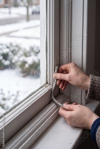 Pressing removable rope caulk into a drafty wooden window for winter energy efficiency