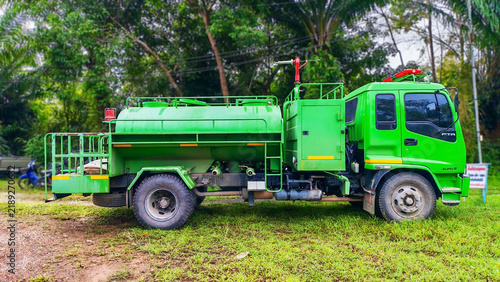 Green water truck parked on grass with trees in background.