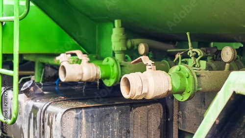 Close-up of water discharge valves and pipe connections on green water truck: A close-up view of industrial piping and valves on a green industrial vehicle.