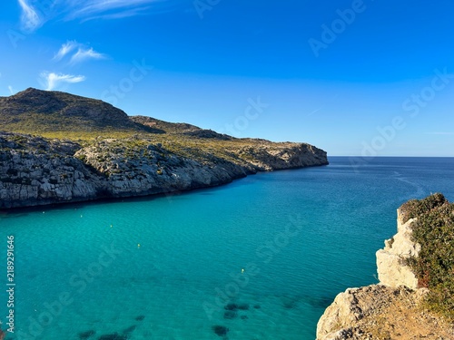 view over the bay Cala Barques with turqouise water towards the Mediterranean Sea near Cala Sant Vicenc in northeastern Mallorca, rocky cliff and the Serra de Tramuntana mountains behind, Spain
