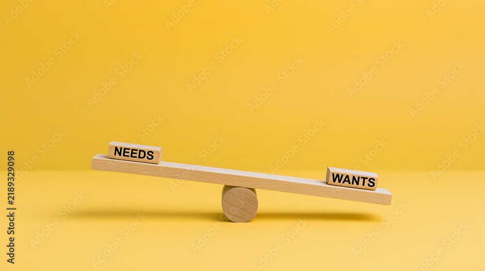 © twc - A conceptual wooden seesaw balance scale contrasting text blocks labeled needs and wants on a minimalist vibrant solid yellow background studio