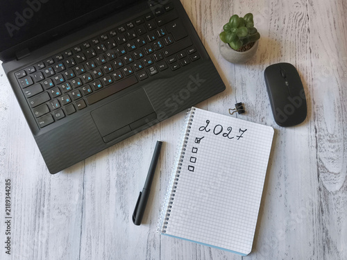Top view of a laptop, notebook with 2027 handwritten goals, pen, mouse and succulent on a rustic wooden desk, symbolizing New Year planning, productivity and organization.