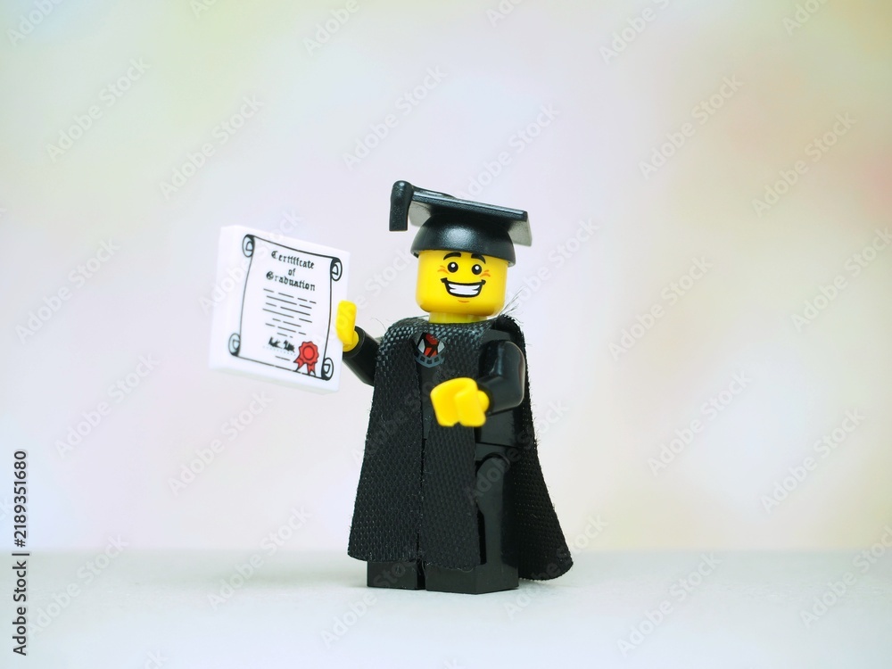 Obraz premium Indonesia - November 24, 2025 : Mini toy of action figure at table with blurred background. Miniature photography concept design. Minifigure of student with graduation gown, cap and certificate.