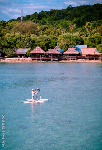 View of couple of tourist are enjoy on water sport paddle sup-board with kayaking along at the edge of the sea beach under crystal clear of water in the island of summer trip