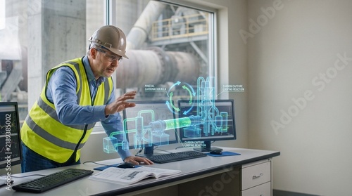 Industrial engineer in hard hat and safety vest analyzing a 3D holographic model of a carbon capture kiln and mineral carbonation looping reaction inside a plant control room
