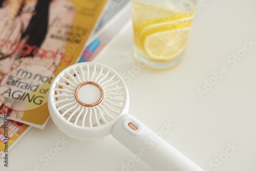 Mini fan, magazines and drink on white table, closeup