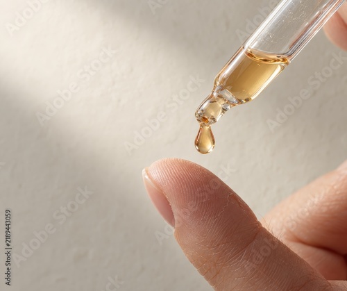 Woman releases the serum drop the moment it falls from the pipette onto her waiting fingertip, facial serum application with copy space