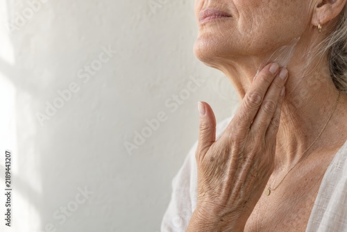 Senior woman applies cream to her neck the moment the back of her hand sweeps upward, mature skin care with copy space