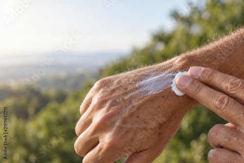Man spreads sunscreen the moment the white streak still shows on his tanned hand, sun protection in daily life with copy space