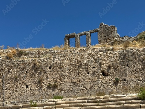 Quadro su tela Scenic view of the Ancient City of Sillyon in Antalya, Turkey, featuring weathered stone walls, historic ruins, and ancient architectural arches against a clear blue sky