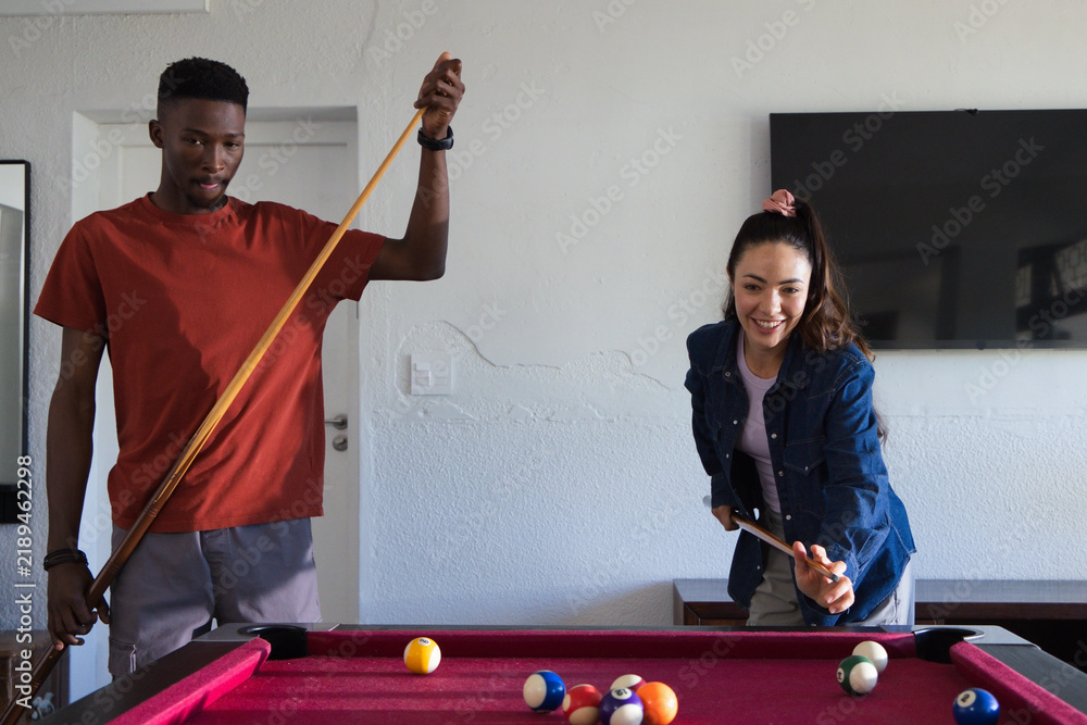 Obraz premium Diverse couple playing pool in home game room on red-felt table with cues and balls