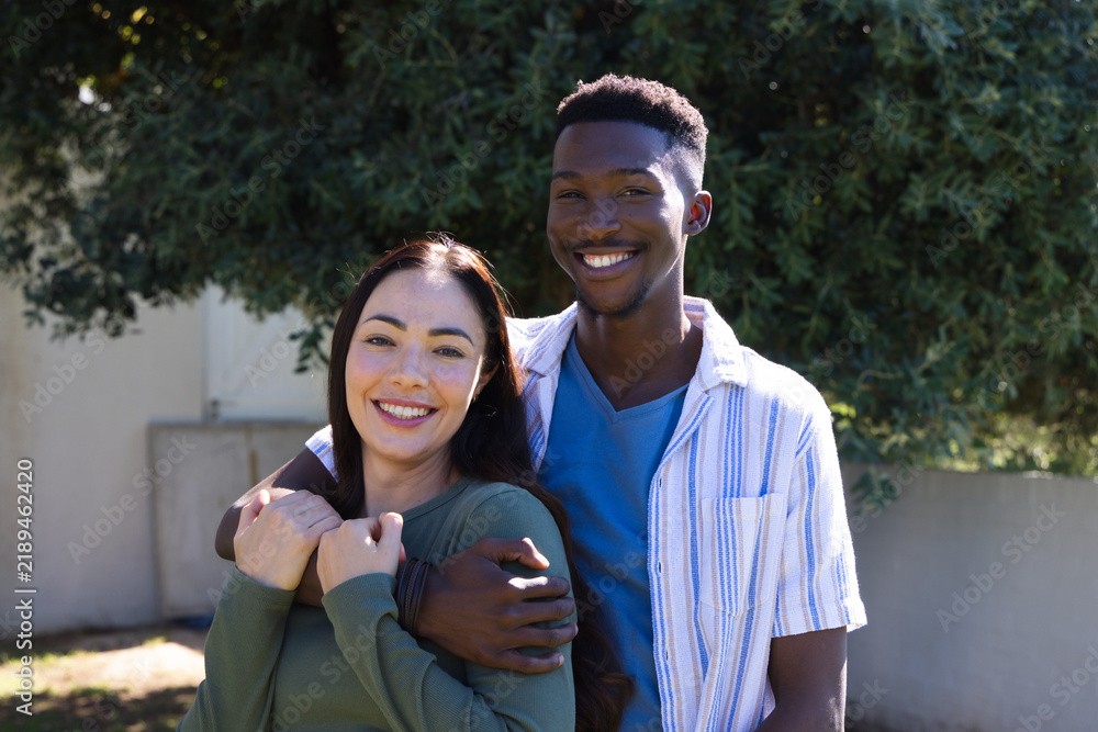 Obraz premium Diverse couple posing outside in yard by pine tree and concrete wall wearing casual clothing