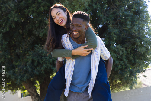 Bild auf Leinwand Couple carrying woman piggyback, smiling under evergreen tree near concrete wall