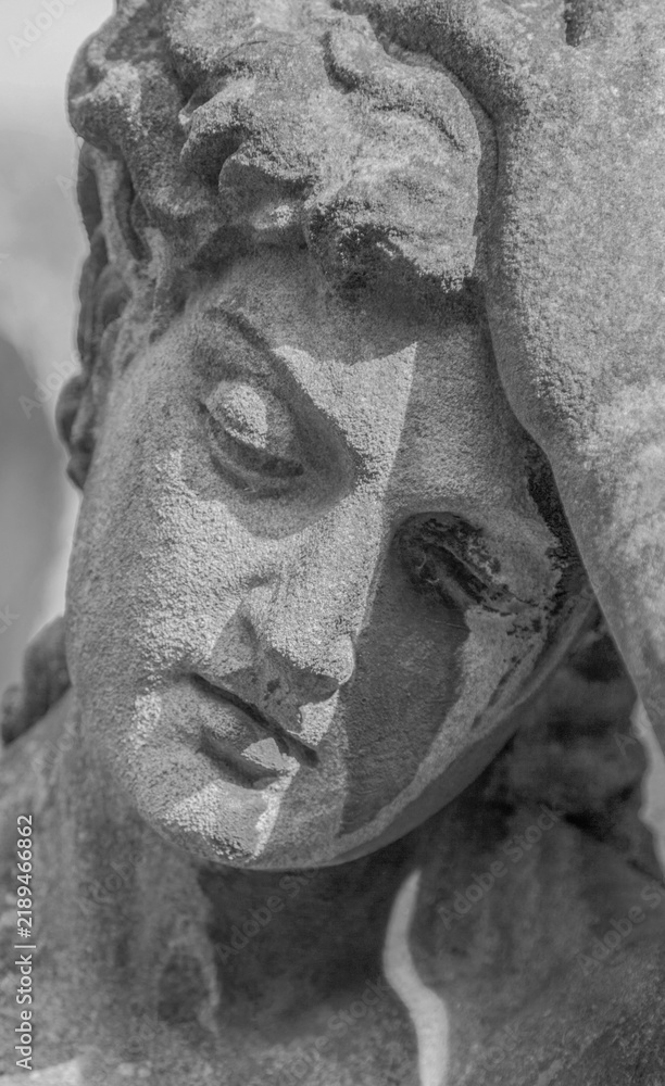 Fototapeta premium Close-up of a sorrowful stone angel statue, symbolizing grief, mourning, loss and remembrance.