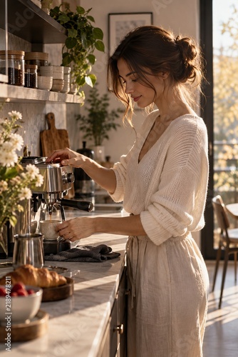 Young woman preparing fresh espresso with a coffee machine in a cozy modern kitchen illuminated by warm natural morning sunlight.