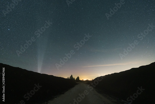 A dirt road running between large peat piles at a night extraction site near Omma bog in Estonia, under a starry sky with a vertical light beam.