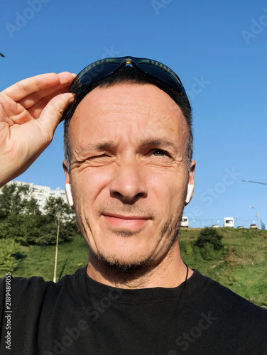 Confident middle-aged man adjusting sunglasses outdoors on a sunny day