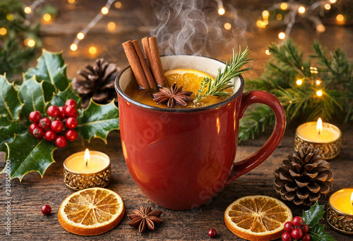 Steaming hot mulled wine in a red mug with cinnamon sticks and orange slices