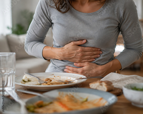 Woman clutches stomach after meal experiencing discomfort at a dining table indoors