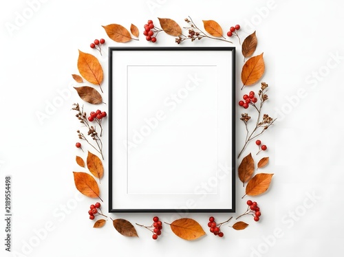 Empty black picture frame surrounded by autumn leaves and red berries on a white background