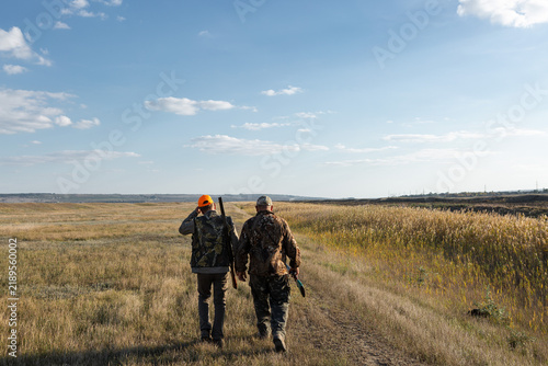 Mature man hunter with gun while walking on field.