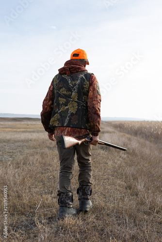 Mature man hunter with gun while walking on field.