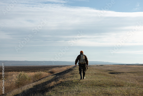 Mature man hunter with gun while walking on field.