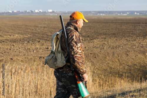 Mature man hunter with gun while walking on field.