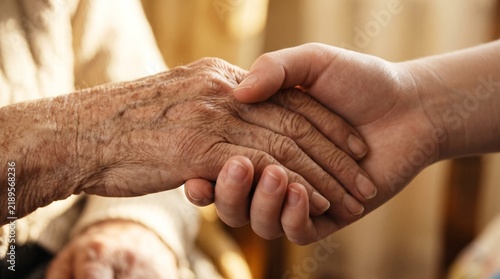 Young person holding wrinkled elderly hand with care and compassion