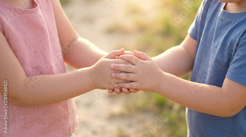 Two children holding hands together in sunny outdoor field at sunset