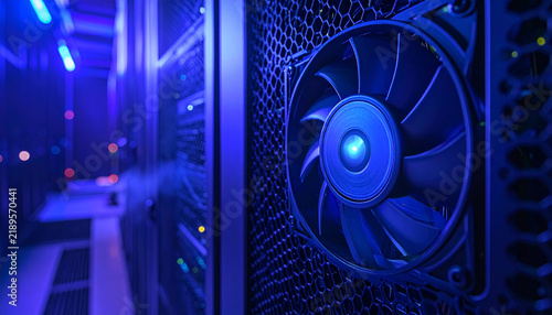 Server Cooling Fan with Blue Light: A close-up of a server room cooling fan with blue LED lights, highlighting the technological infrastructure and cooling system of data centers.