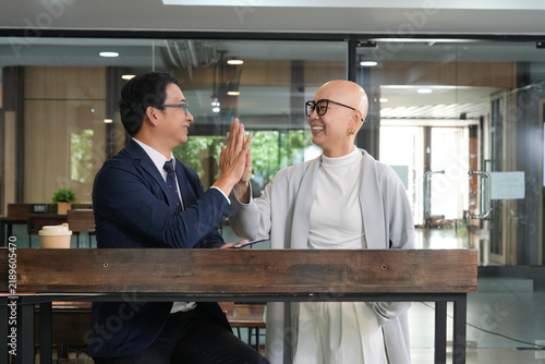 Принти на полотні A bespectacled Korean woman stands greeting and chatting with a male colleague—a businessman in a suit and glasses—as they shake hands in a coworking space café