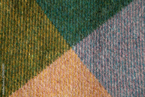 Close-up of authentic vintage wool cashmere with geometric color-block pattern in green, blue, yellow and muted pink. Soft textured woven fabric with natural fibers and rich color transitions. 