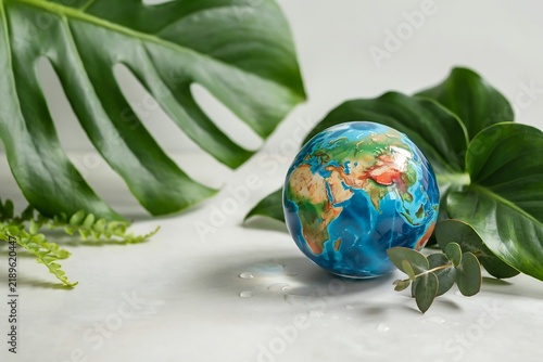 Crystal world globe resting on a stone surface surrounded by large tropical palm leaves with tropical environment sustainability conservation protection earthday environmental botanical