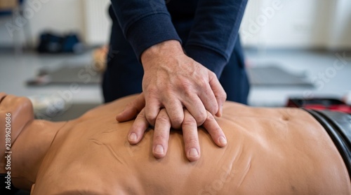 Close-up of hands performing CPR chest compressions on a medical training mannequin during a first aid class