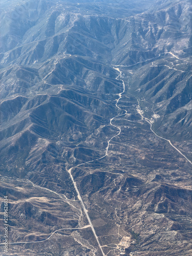 Aerial view of a rugged canyon with a pale riverbed snaking between forested ridge lines and a straight road below, Acton, California