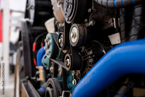 Side close-up view of alternator, belt tensioner pulleys, and blue hoses in a heavy vehicle engine bay.